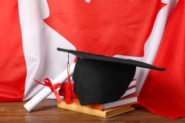Mezuniyet şapkası, diploma, kitap ve Kanada bayrağı ahşap masada.