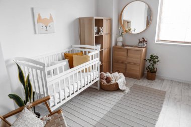 Bebek beşiği, çekmecesi ve aynası olan aydınlık yatak odasının içinde.