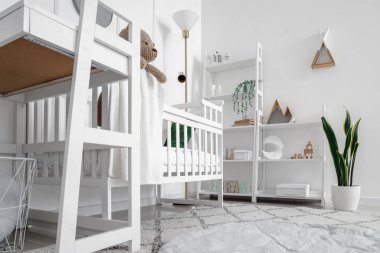 Bebek karyolası, masa ve raf değiştirme ünitesiyle aydınlık yatak odasının içinde.