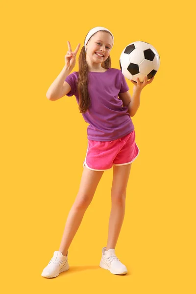 Sportief Klein Meisje Met Voetbal Tonen Overwinning Gebaar Gele Achtergrond — Stockfoto