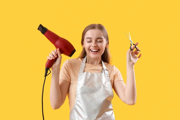 黄色の背景に乾燥機とはさみ付きの女性の美容師 — ストック写真
