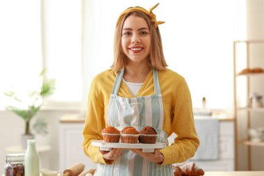 Female baker with tray of tasty cupcakes in kitchen