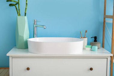 Lavabo, banyo aksesuarları ve mavi duvarın yanındaki çekmecelerde bambu saplı vazolar.