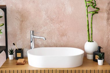 Masada bambu saplı lavabo, banyo aksesuarları ve vazo var.