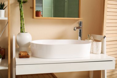 Masada beyaz lavabo, banyo aksesuarları ve bambu saplı vazo var.