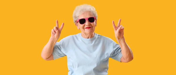 Stilvolle Seniorin Mit Sonnenbrille Zeigt Siegesgeste Auf Gelbem Hintergrund — Stockfoto