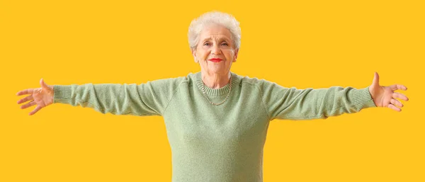 Yeşil Kazaklı Yaşlı Kadın Sarı Arka Planda Kolları Açık — Stok fotoğraf