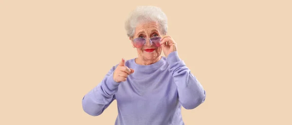 Snygg Senior Kvinna Solglasögon Pekar Betraktaren Beige Bakgrund — Stockfoto