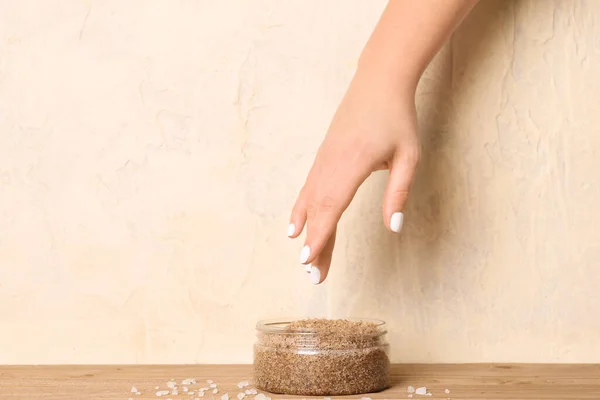Female hand with jar of body scrub on wooden table