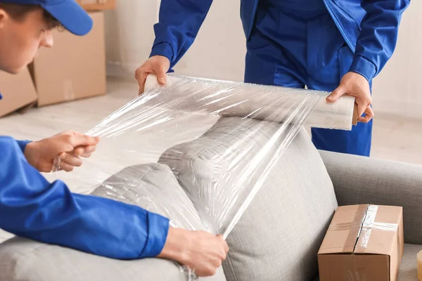 stock image Male movers wrapping sofa with stretch film in room, closeup