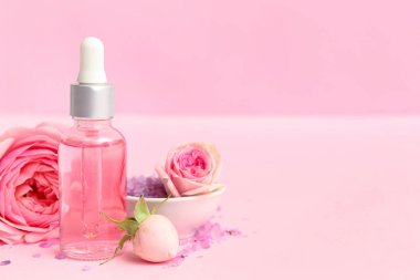 Gül özü ve pembe arka planda çiçekler olan bir şişe kozmetik yağı.