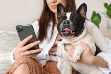 Evde cep telefonu kullanan buldoguyla genç bir kadın.