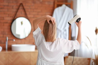 Banyoda saç kurutma makinesi olan güzel bir sarışın.