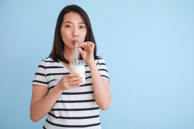 Açık mavi arka planda bir bardak sütle güzel bir Asyalı kadın.