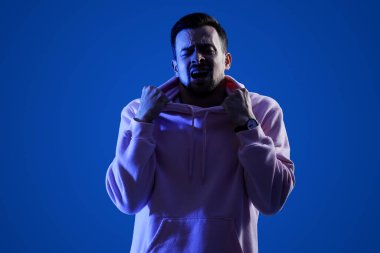 Genç adam mavi arka planda panik atak geçiriyor.