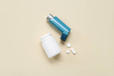 Astım ilacı ve bej arka planda haplarla dolu bir kutu.