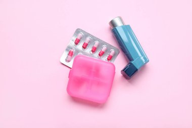 Astım spreyi ve pembe arka planda haplı kutu.