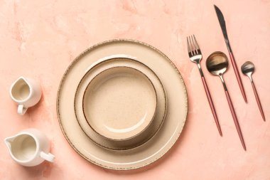 Pembe masada temiz tabak, kase ve çatal bıçak takımı var.