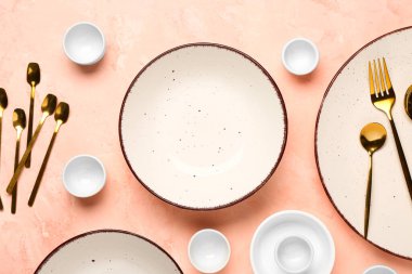 Temiz tabak, kase ve pembe masadaki altın çatal bıçak takımı.