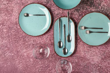 Temiz tabaklar, bardaklar ve koyu pembe masadaki çatal bıçak takımı.