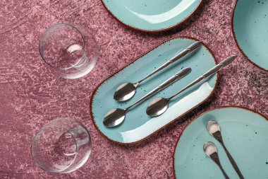 Temiz tabaklar, bardaklar ve koyu pembe masadaki çatal bıçak takımı.