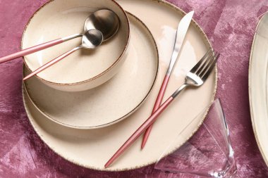 Koyu pembe masada temiz tabak, kase ve çatal bıçak takımı.