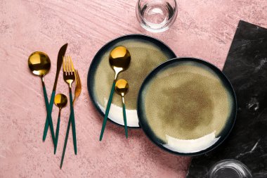 Koyu pembe masada temiz tabaklar ve altın çatal bıçak takımı.