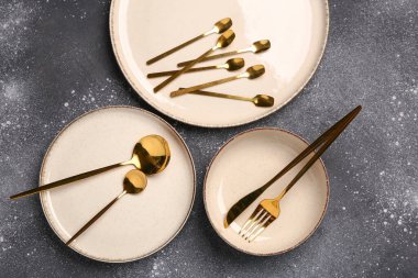 Koyu gri masada temiz tabak, kase ve altın çatal bıçak takımı.