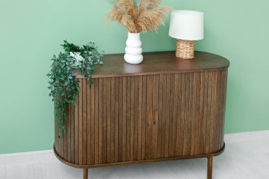 Çimenli ahşap çekmeceler, ev bitkisi ve lamba yeşil duvarın yanında.