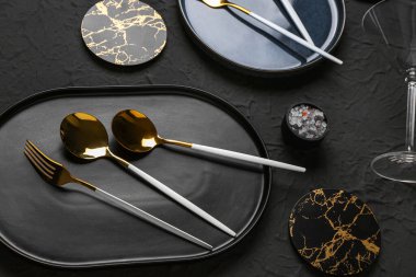 Temiz tabak, bardak altlığı, çatal ve kaşıklar siyah masada.