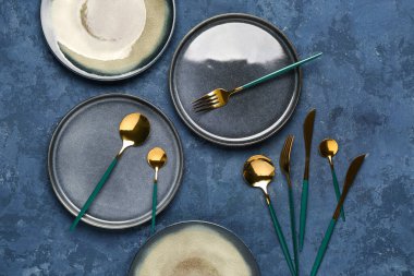 Mavi grunge arkaplan üzerinde temiz tabaklar ve altın çatal bıçak seti ile masa ayarları