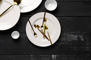 Siyah ahşap masanın üzerinde altın çatal bıçak takımı olan temiz tabaklar.