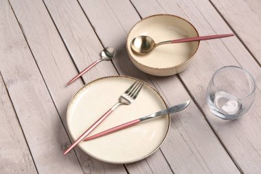 Temiz tabak, kase, çatal bıçak takımı ve gri ahşap masada bir bardak su.