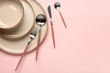 Masa seti, temiz tabaklar, kase ve pembe arka planda çatal bıçak takımı.