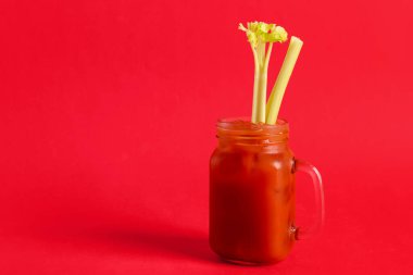 Kırmızı zemin üzerinde kereviz olan bir kavanoz Bloody Mary.