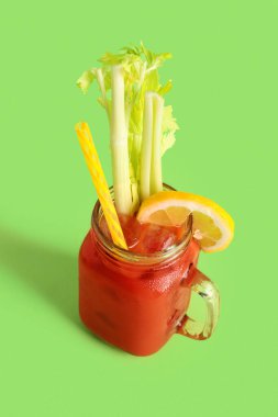 Yeşil zemin üzerinde kereviz ve limon olan bir kavanoz Bloody Mary.