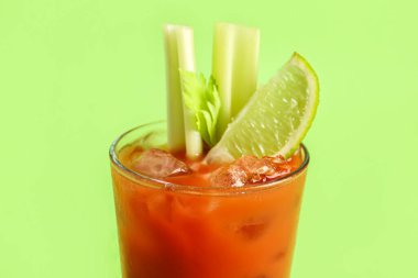 Yeşil zemin üzerinde kereviz ve limon olan bir bardak Bloody Mary.