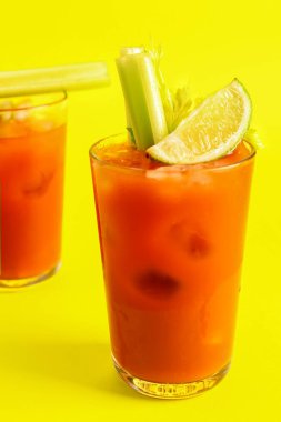 Sarı arka planda kereviz ve limonlu Bloody Mary bardakları.