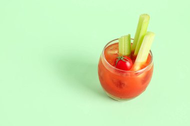 Yeşil arka planda kereviz ve domatesli bir bardak Bloody Mary.