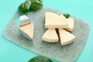 Turkuaz arka planda lezzetli işlenmiş peynir ve fesleğen yaprakları olan tahta, yakın plan.