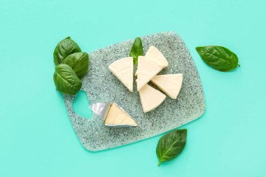 Turkuaz arka planda lezzetli işlenmiş peynir ve fesleğen yaprakları olan tahta