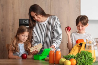 Anne küçük çocukları için mutfakta öğle yemeği hazırlıyor.