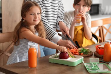 Anne, küçük çocuklarına mutfakta öğle yemeği hazırlıyor.