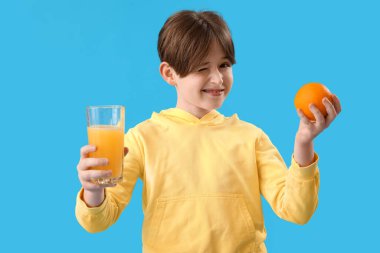 Mavi arka planda portakal suyu ve bir bardak meyve suyu olan küçük çocuk.