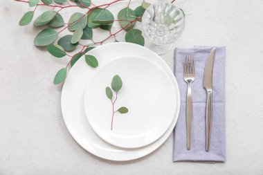 Gri masa üzerinde temiz tabak, çatal bıçak takımı ve okaliptüs dallarıyla güzel bir masa.