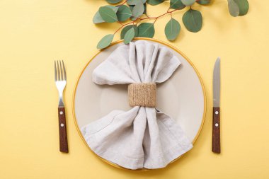 Sarı arka planda katlanmış peçete ve okaliptüs dallarıyla güzel bir masa.