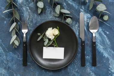 Boş davetiye kartı, östoma çiçeği ve mavi masadaki okaliptüs dallarıyla güzel bir masa.