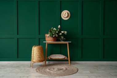 Yeşil duvarın yanındaki konsol masasında yasemin çiçekleri açan Hasır sepet.