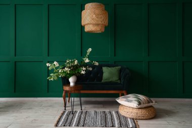 Sehpanın üzerinde yasemin çiçekleri ve yeşil duvarın yanında kanepe olan vazo.