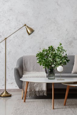 Oturma odasının içinde rahat gri kanepe ve kahve masasında çiçek açan yasemin çiçekleri.